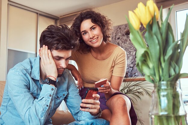 Una pareja hispana relajándose juntos en el sofá. Usando teléfonos inteligentes mientras descansa en casa en la sala de estar.