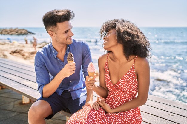 Pareja de hombre y mujer sonriendo confiada usando un teléfono inteligente en la playa
