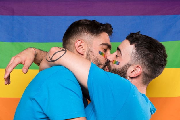 Pareja de hombres homosexuales abrazándose y besándose en la bandera del arco iris