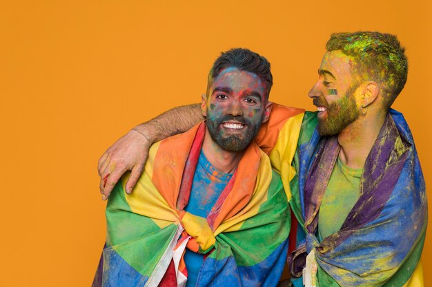 Pareja de hombres homosexuales cubiertos por la bandera LGBT y pintados de colores.
