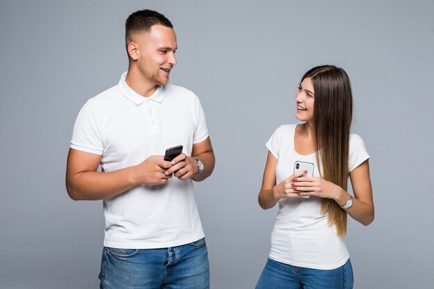 Pareja de hombres y mujeres de pie con teléfonos móviles de marca en sus manos aisladas sobre fondo gris