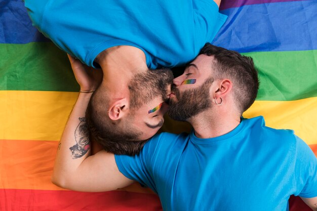 Pareja de hombres tumbados y besándose en bandera LGBT