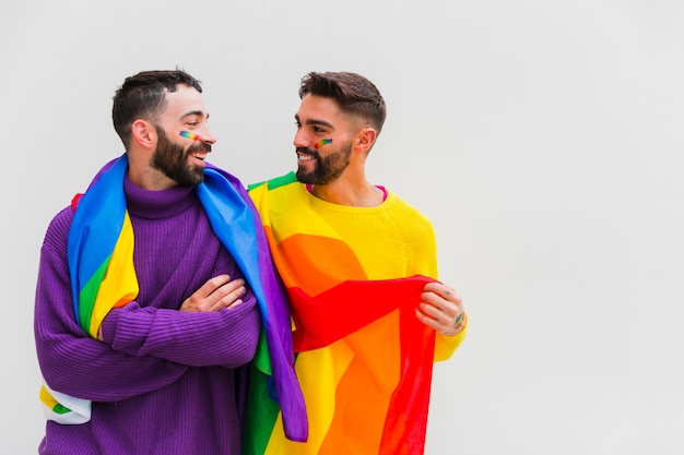 Pareja de homosexuales con banderas LGBT en los hombros sonriendo juntos