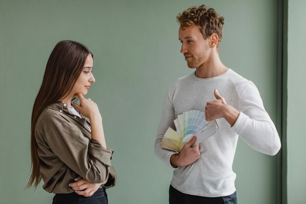 Pareja indecisa discutiendo la redecoración de la casa con paleta de pintura