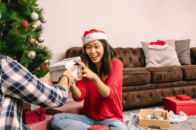 Pareja intercambiando caja de regalo al lado de árbol de navidad