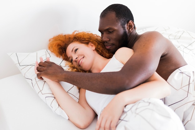 Foto gratuita pareja interracial tomados de la mano en la cama