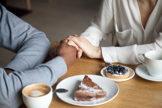 Pareja interracial tomados de la mano sentado en la mesa de café, vista de cerca