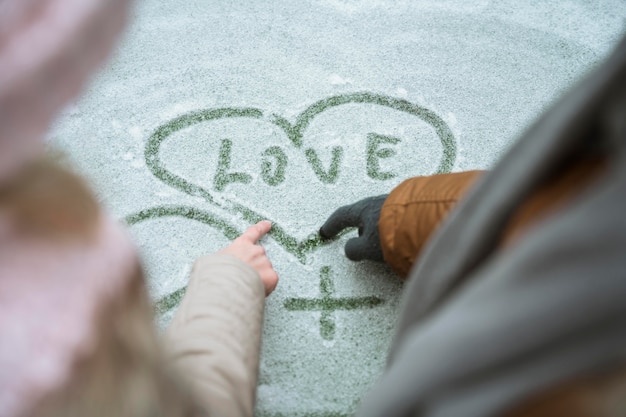 Pareja en invierno escribiendo amor en la nieve.