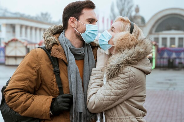 Pareja en invierno con máscaras médicas y abrazos