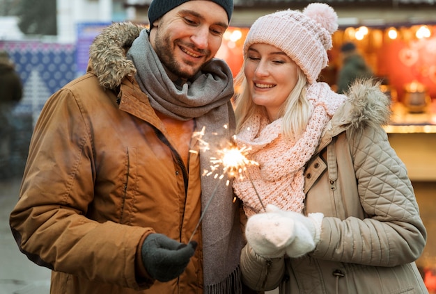 Pareja en invierno mujer sosteniendo destellos de fuegos artificiales