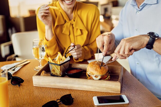 Pareja irreconocible comiendo hamburguesas y amigos franceses en un restaurante
