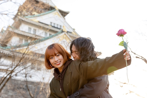 Pareja japonesa abrazada al aire libre mientras su novia sostiene una rosa