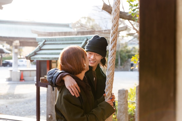 Una pareja japonesa sonriente aferrándose a una cuerda del templo