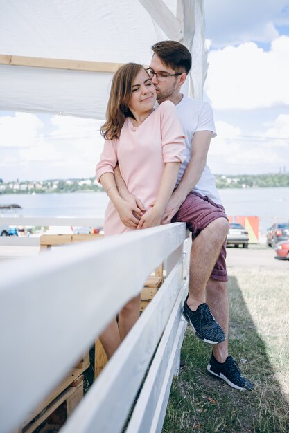 Foto gratuita pareja joven abrazada y sentada en una valla blanca