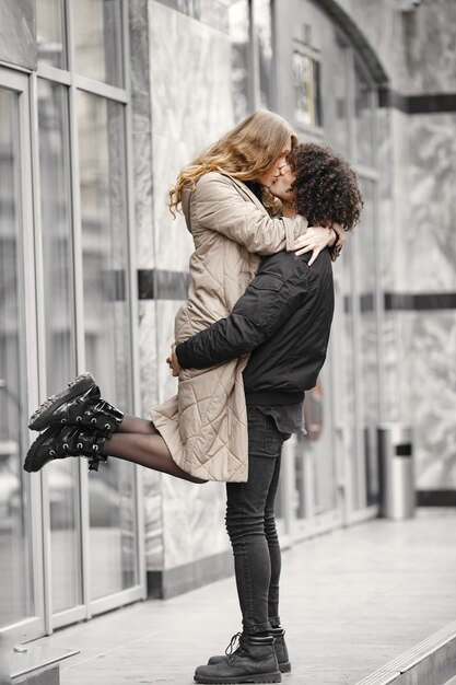 Pareja joven abrazándose y besándose en la calle vistiendo abrigos.