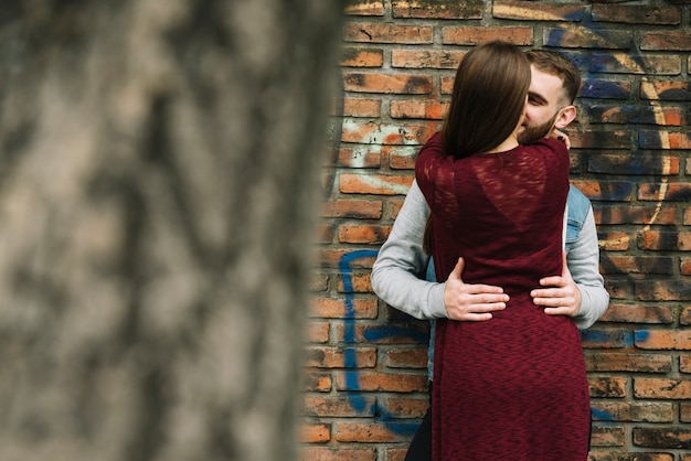 Pareja joven abrazándose enfrente de pared de ladrillo