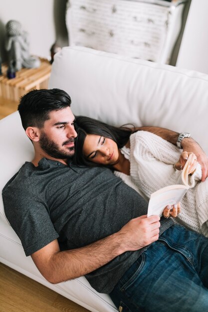 Pareja joven, acostado, en, sofá blanco, libro de lectura