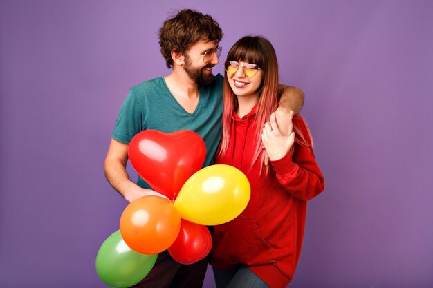 Pareja joven adorable posando en la pared violeta con globos