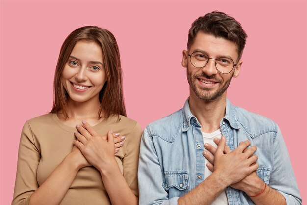 pareja joven agradecida posando contra la pared rosa