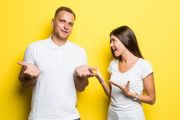 Pareja joven aislado sobre fondo amarillo tienen una conversación juntos vestidos con camisetas blancas