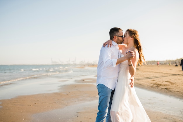 Pareja joven amorosa cogidos de la mano unos a otros besándose en la playa de verano