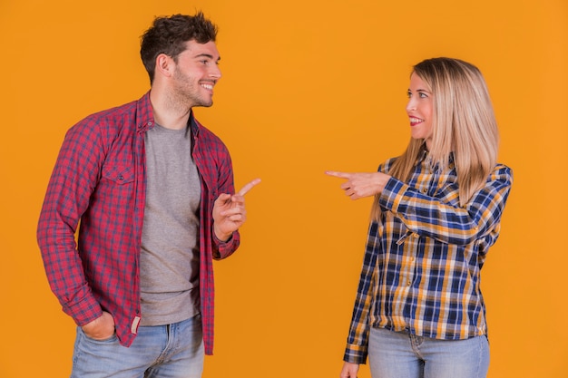 Foto gratuita pareja joven apuntando sus dedos entre sí contra un fondo naranja