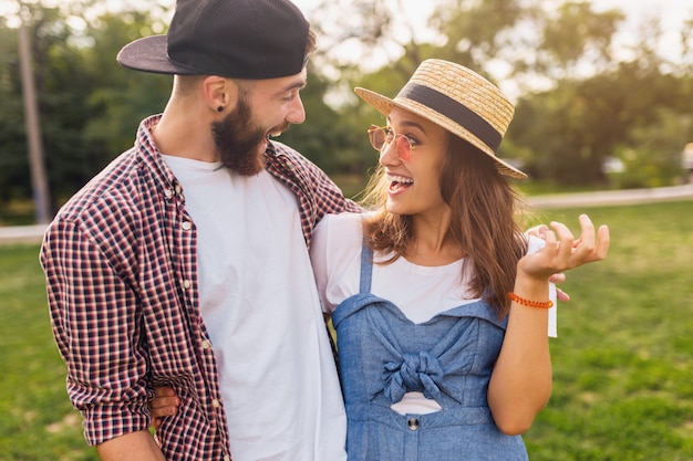 Pareja joven bastante hipster caminando en el parque hablando riendo, amigos divirtiéndose juntos, romance en la fecha, estilo de moda de verano, traje de hipster colorido, hombre y mujer sonriendo abrazándose