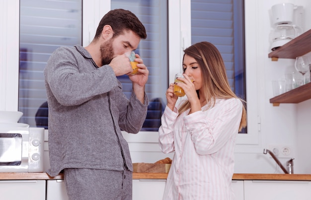 Foto gratuita pareja joven bebiendo jugo de naranja en la cocina