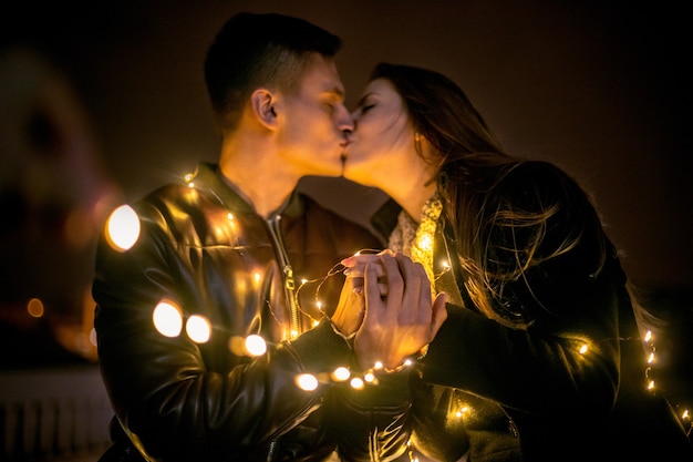 Pareja joven besándose y abrazándose al aire libre en la calle de noche en Navidad