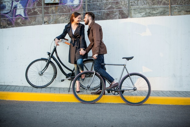 Foto gratuita pareja joven con una bicicleta frente a la ciudad