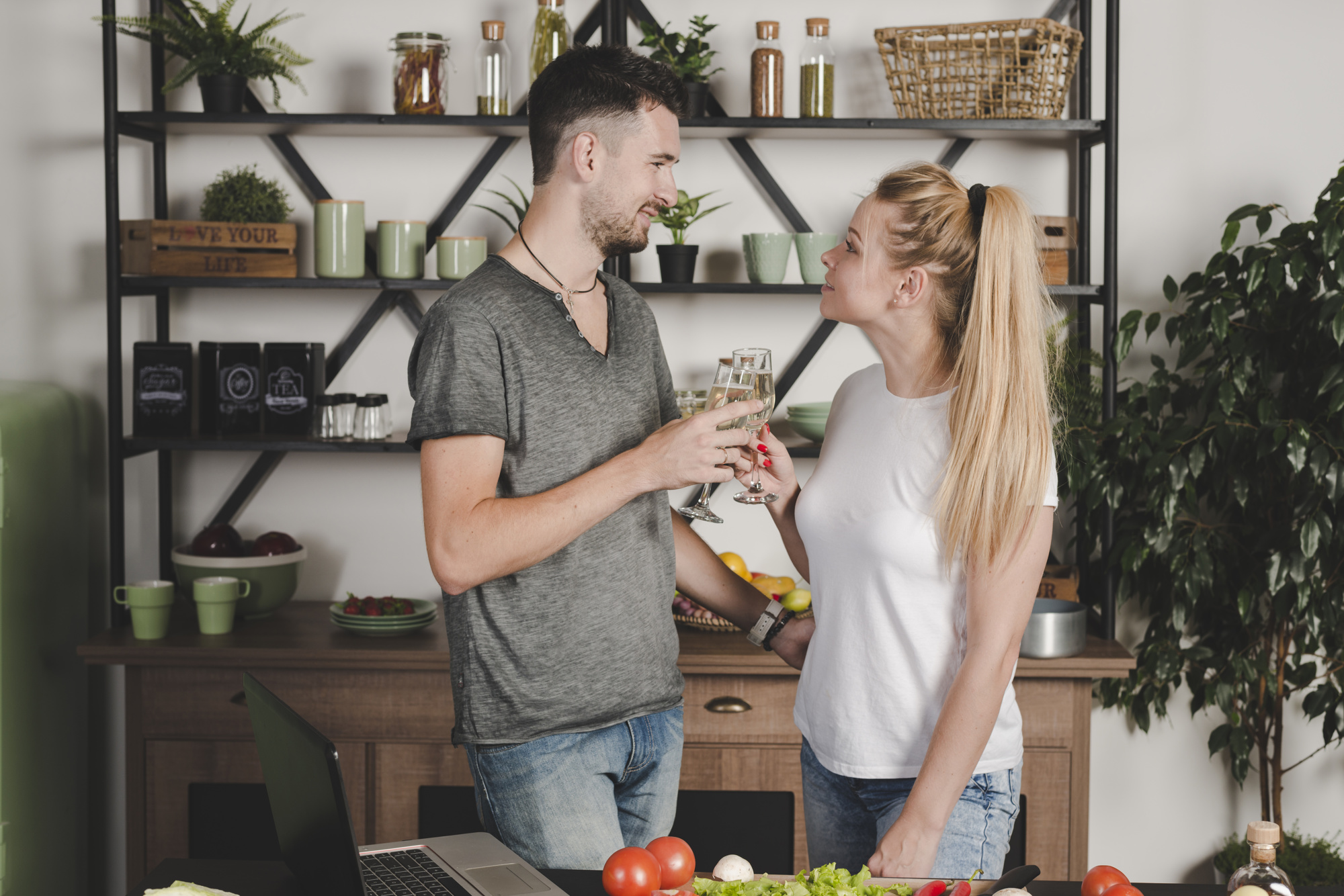 Pareja joven brindando champán flauta parado en la cocina