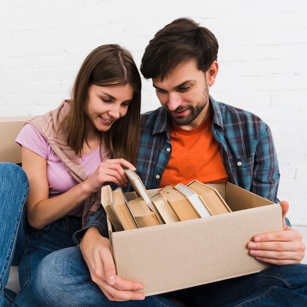 Foto gratuita pareja joven buscando libros en la caja de cartón