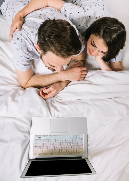 Pareja joven en la cama usando portátil