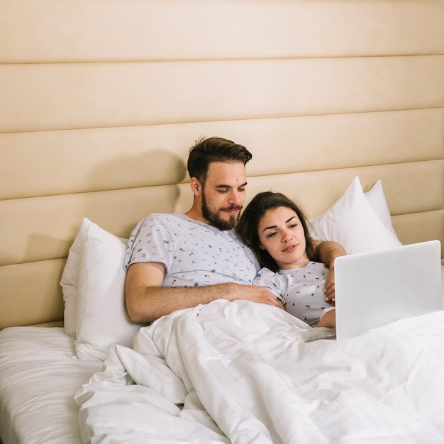 Pareja joven en la cama usando portátil