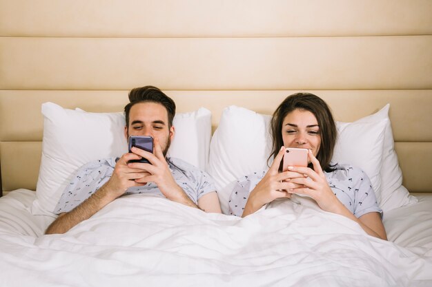 Pareja joven en la cama usando smartphones