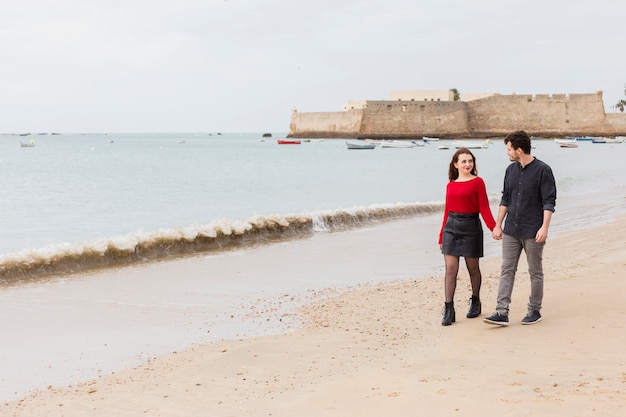 Foto gratuita pareja joven caminando en la orilla del mar de arena