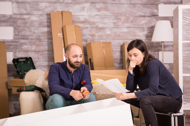 Pareja joven caucásica montaje de muebles en apartamento nuevo. Instrucciones de lectura de la novia.