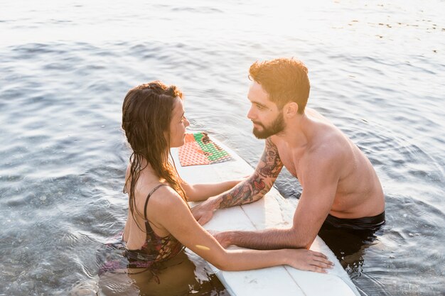 Pareja joven cerca de la tabla de surf en el mar