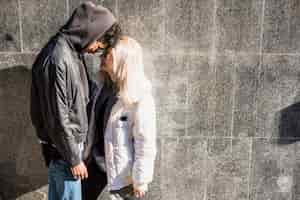 Foto gratuita pareja joven con chaqueta de pie contra la pared gris tocando su frente