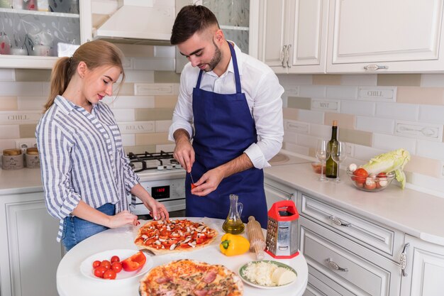 Pareja joven cocinando pizza con verduras y champiñones