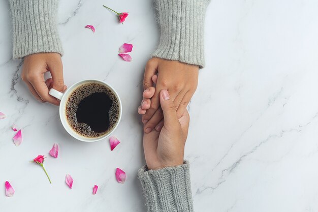 Pareja joven cogidos de la mano para comer café en una mesa de madera.