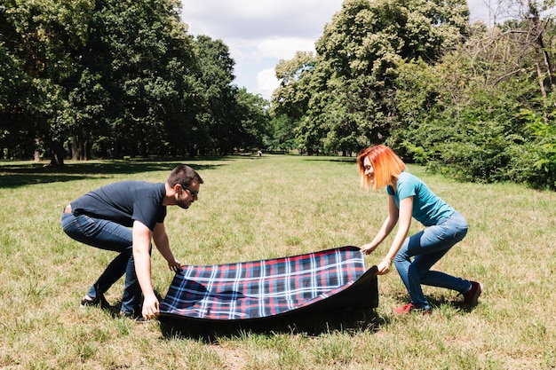 Pareja joven colocando una manta en la hierba verde en el parque