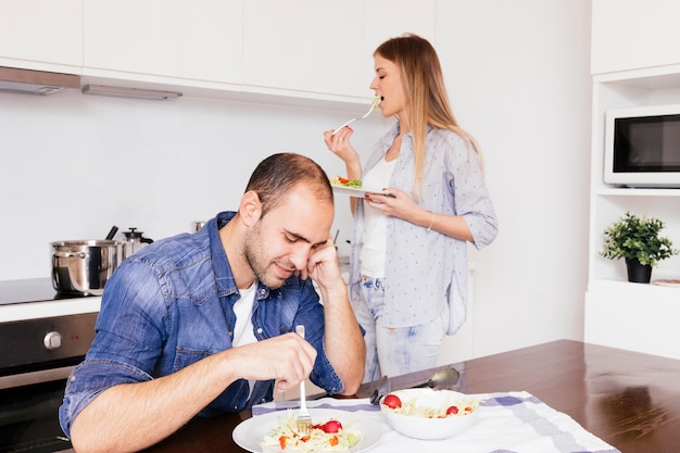 Pareja joven comiendo ensalada en la cocina