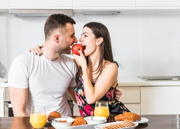 Pareja joven comiendo manzana con desayuno en mesa de madera