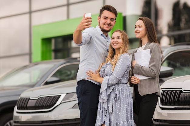 Pareja joven y concesionario de automóviles tomando una selfie