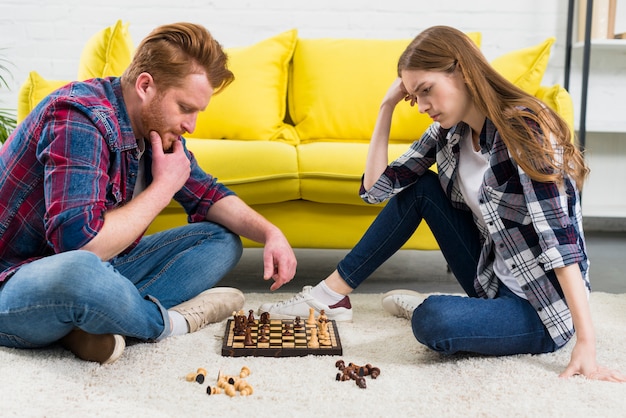 Foto gratuita pareja joven contemplada mirando el juego de ajedrez en la sala de estar