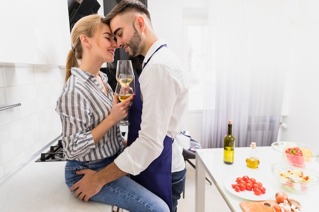 Pareja joven con copas de vino abrazando en cocina