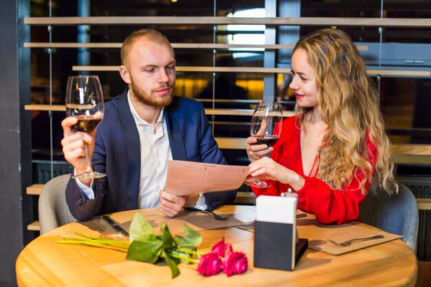 Pareja joven con copas de vino leyendo el menú