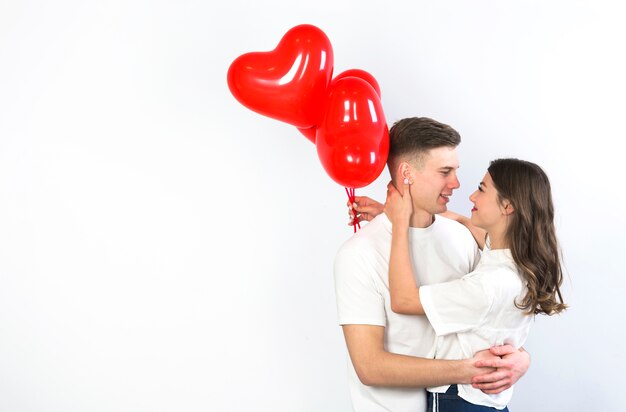 Pareja joven con corazón rojo globos abrazos