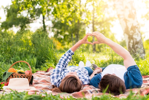 Pareja joven descansando en plaid y mostrando gesto de corazón